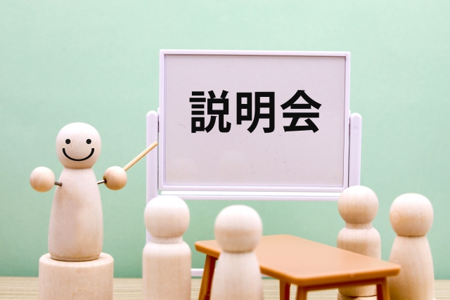 説明会と書かれたホワイトボードを指し示す人形