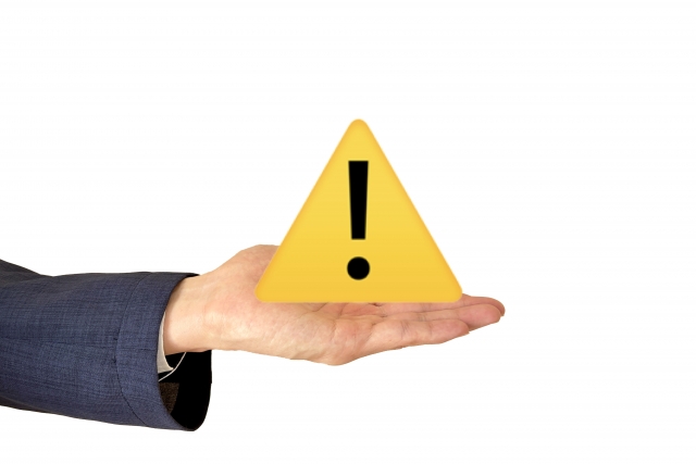 黄色い三角とビックリマークの注意アイコンを手に持つ人